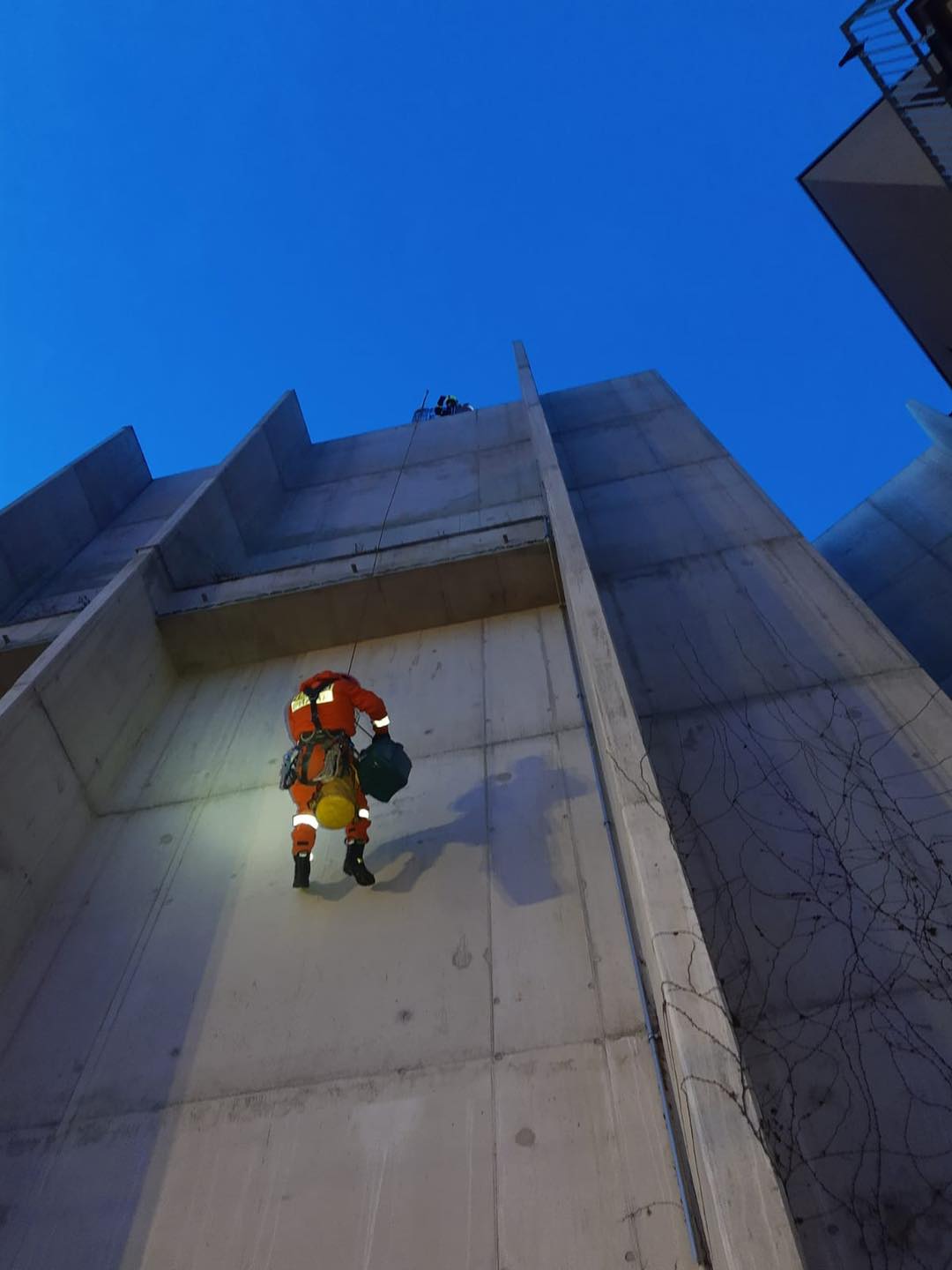 PHA_záchrana poštolky_hasič-lezec se slaňuje z budovy s poštolkou v přepravní kleci.png